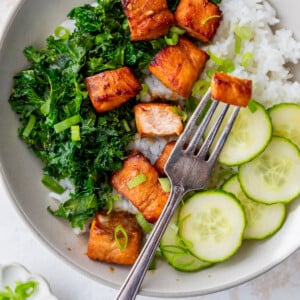 a fork picking up an air fryer salmon bite from a veggie and rice bowl.