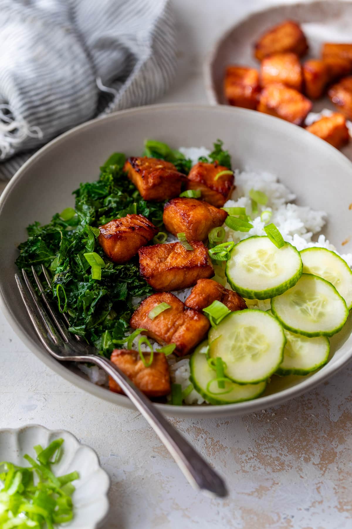air fryer salmon bites on top of a cucumber, kale, and rice bowl.