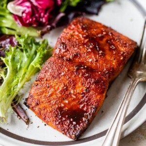 zoomed in image of cooked salmon on a plate with lettuce and a fork