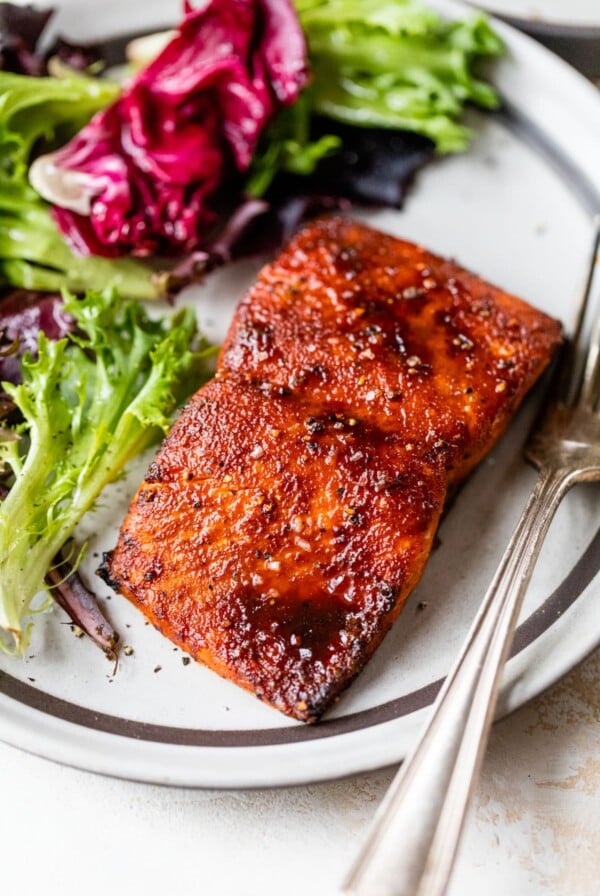 zoomed in image of cooked salmon on a plate with lettuce and a fork