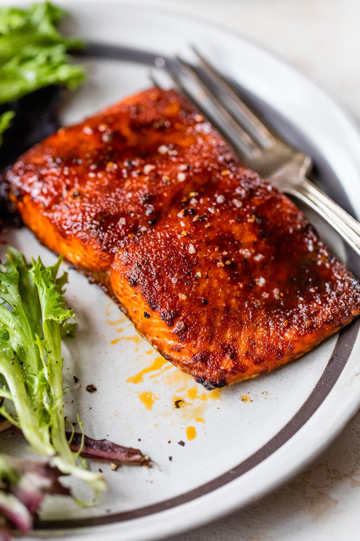 zoomed in image of cooked salmon on a plate with lettuce and a fork