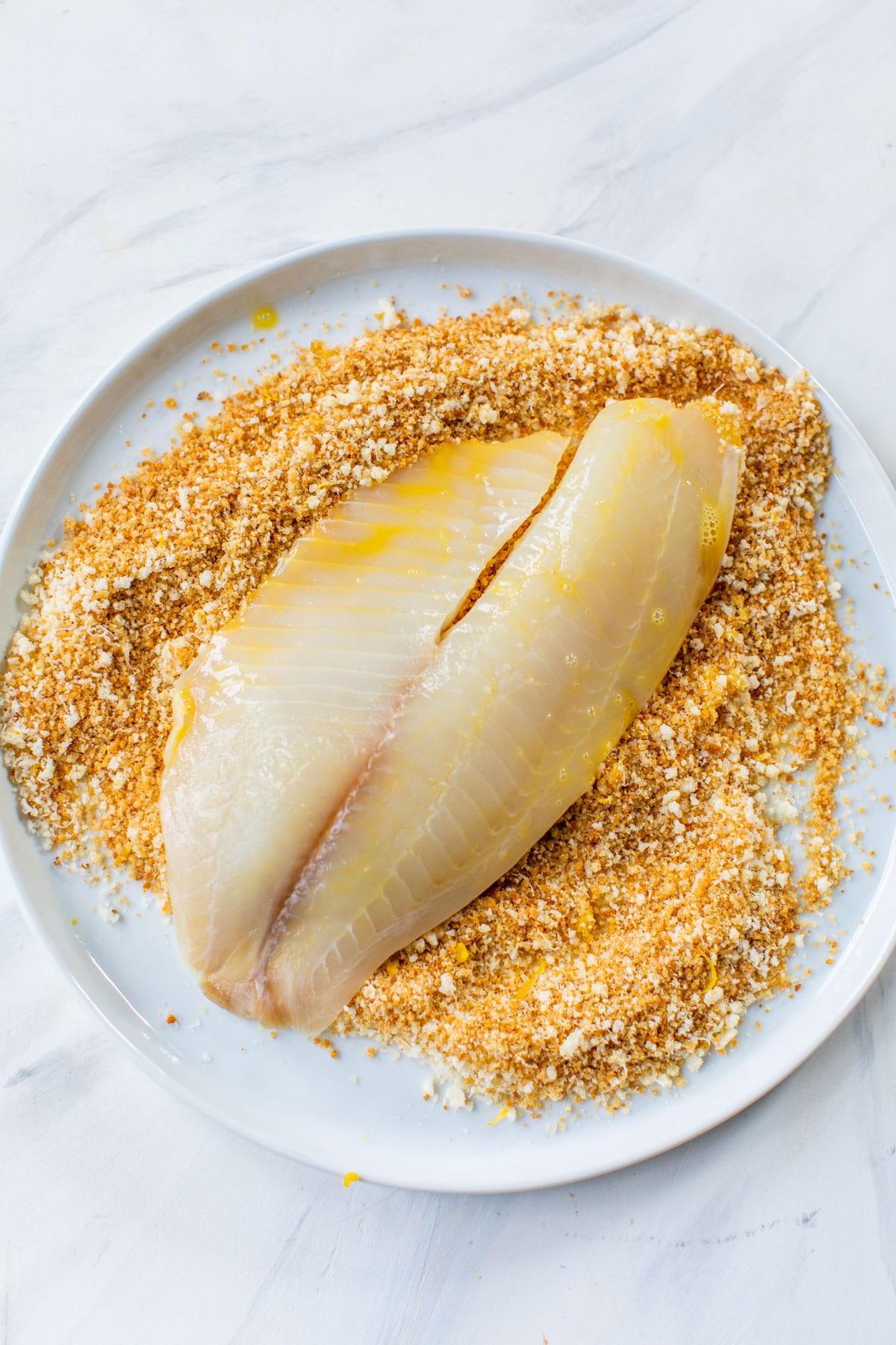 raw piece of fish being dipped in breadcrumbs
