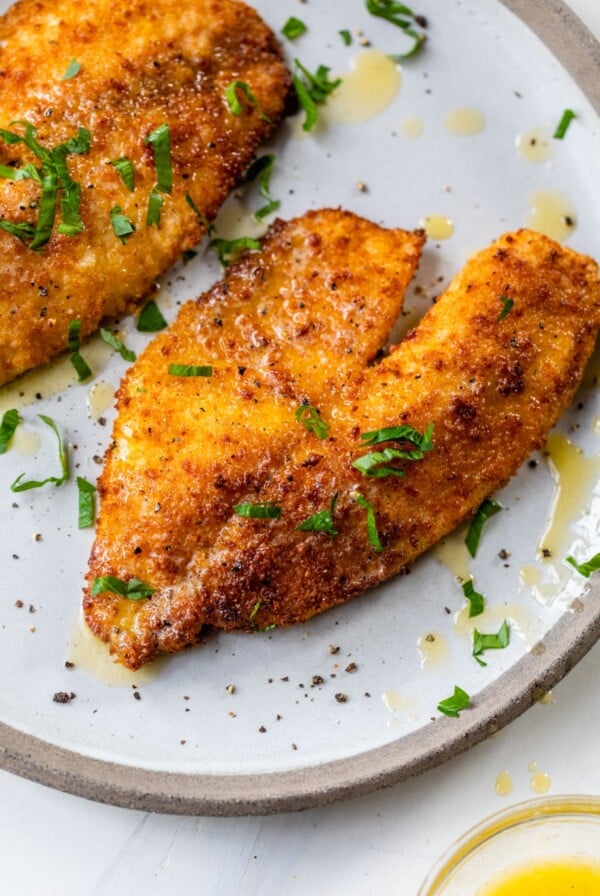 cooked breaded fish on a plate topped with chopped parsley