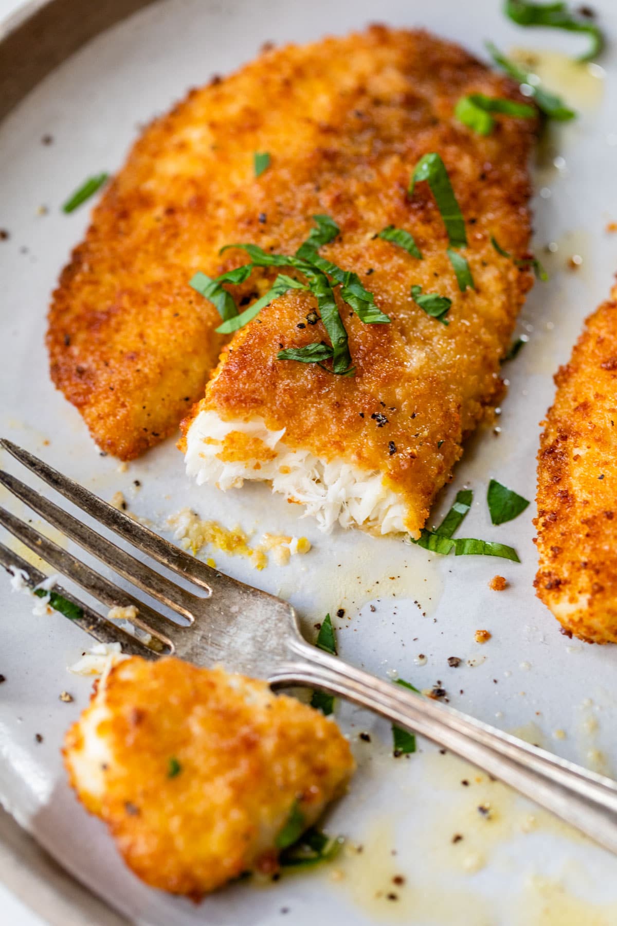 a piece of tilapia on a plate with a bite taken out of it
