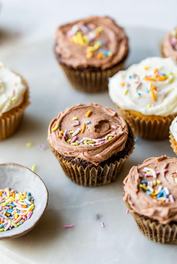 chocolate and vanilla cupcakes topped with rainbow sprinkles on a marble board