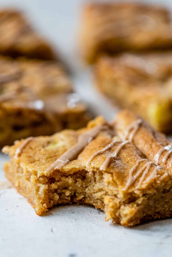 side view of an apple blondie with a bite taken out and with cinnamon glaze drizzled over the top