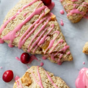 overhead view of 3 apple cranberry scones topped with a drizzle of pink cranberry glaze with fresh cranberries on the side.
