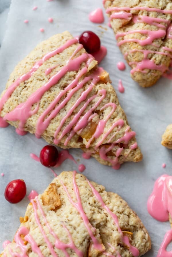 overhead view of 3 apple cranberry scones topped with a drizzle of pink cranberry glaze with fresh cranberries on the side.