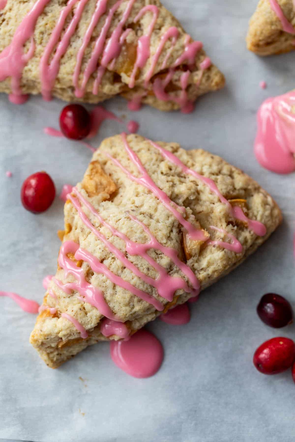 overhead view of 2 apple cranberry scones topped with a drizzle of pink cranberry glaze with fresh cranberries on the side.