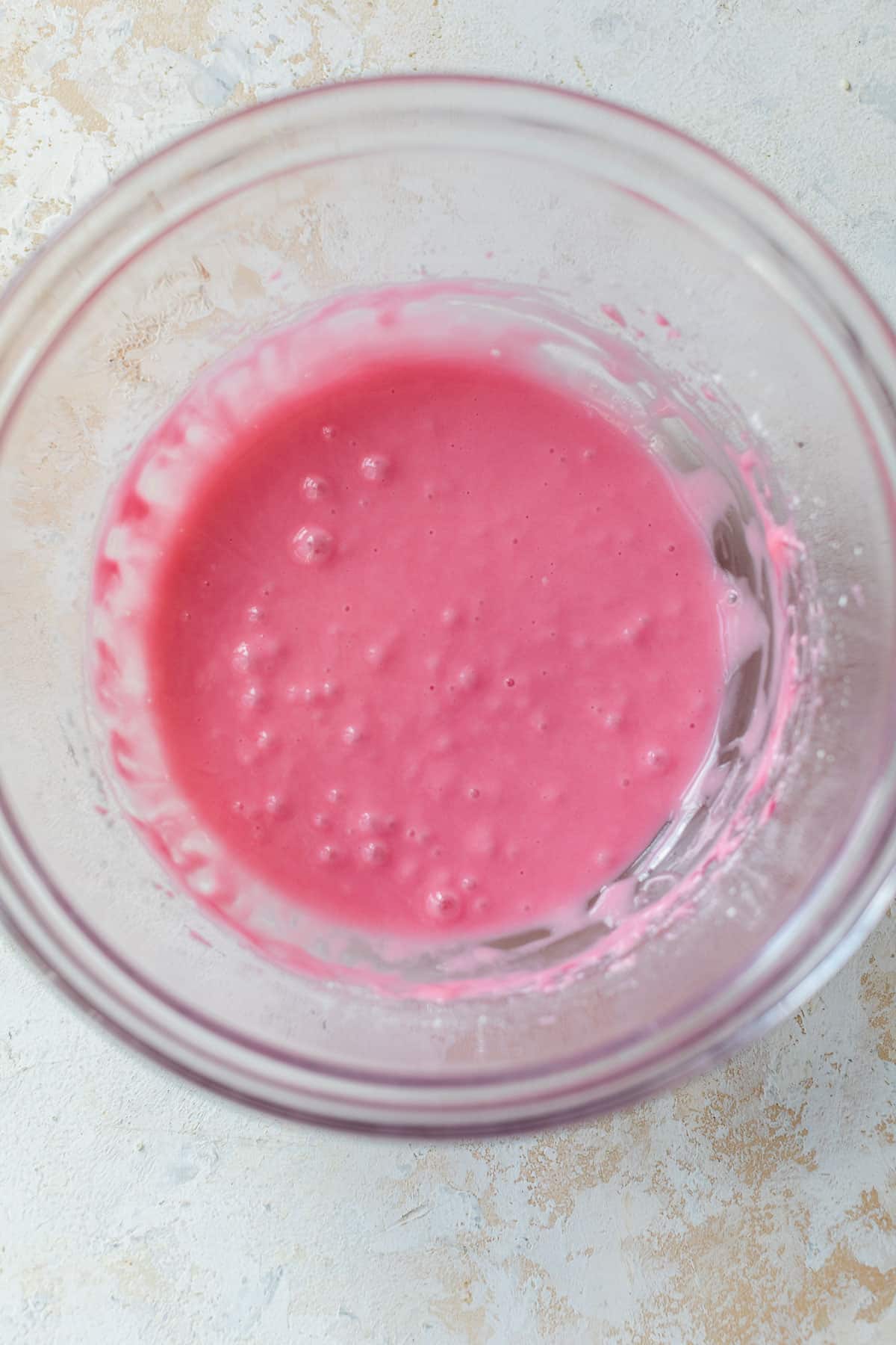 overhead view of smooth and pink cranberry glaze for apple cranberry scones in a glass bowl.