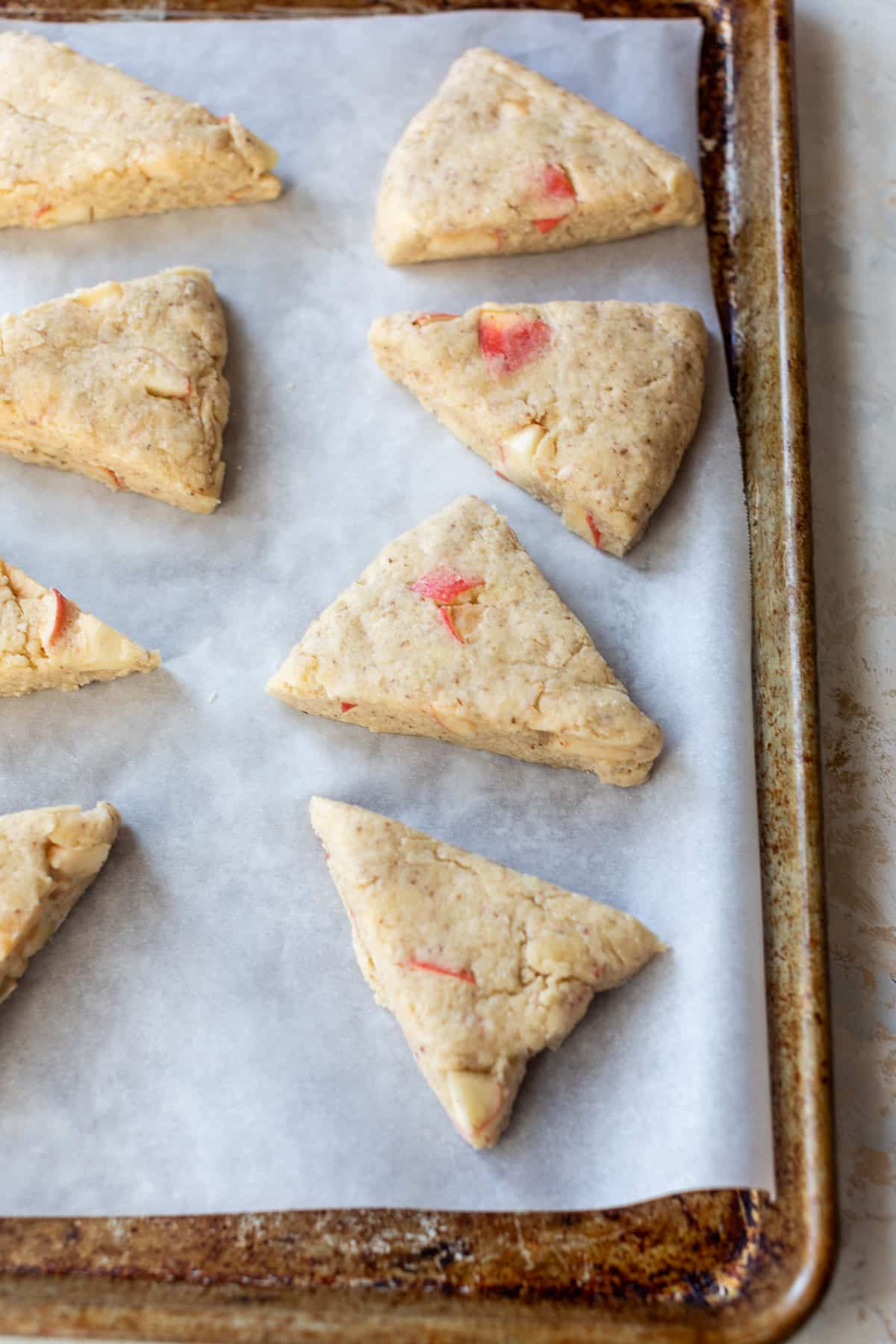side view of 8 unbaked apple cranberry scones on a parchment-lined baking sheet.