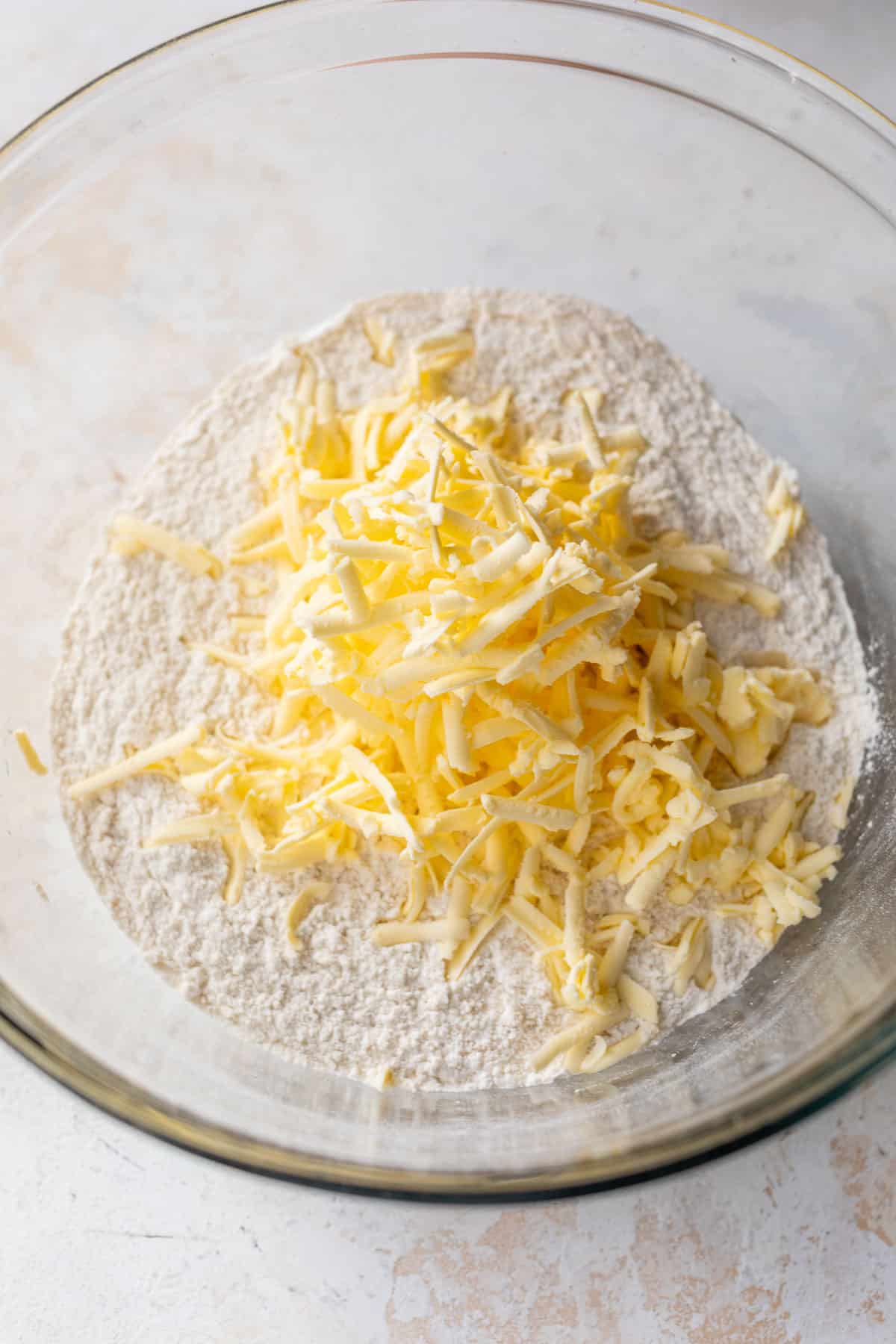 the dry ingredients topped with grated butter for apple cranberry scones in a glass bowl.