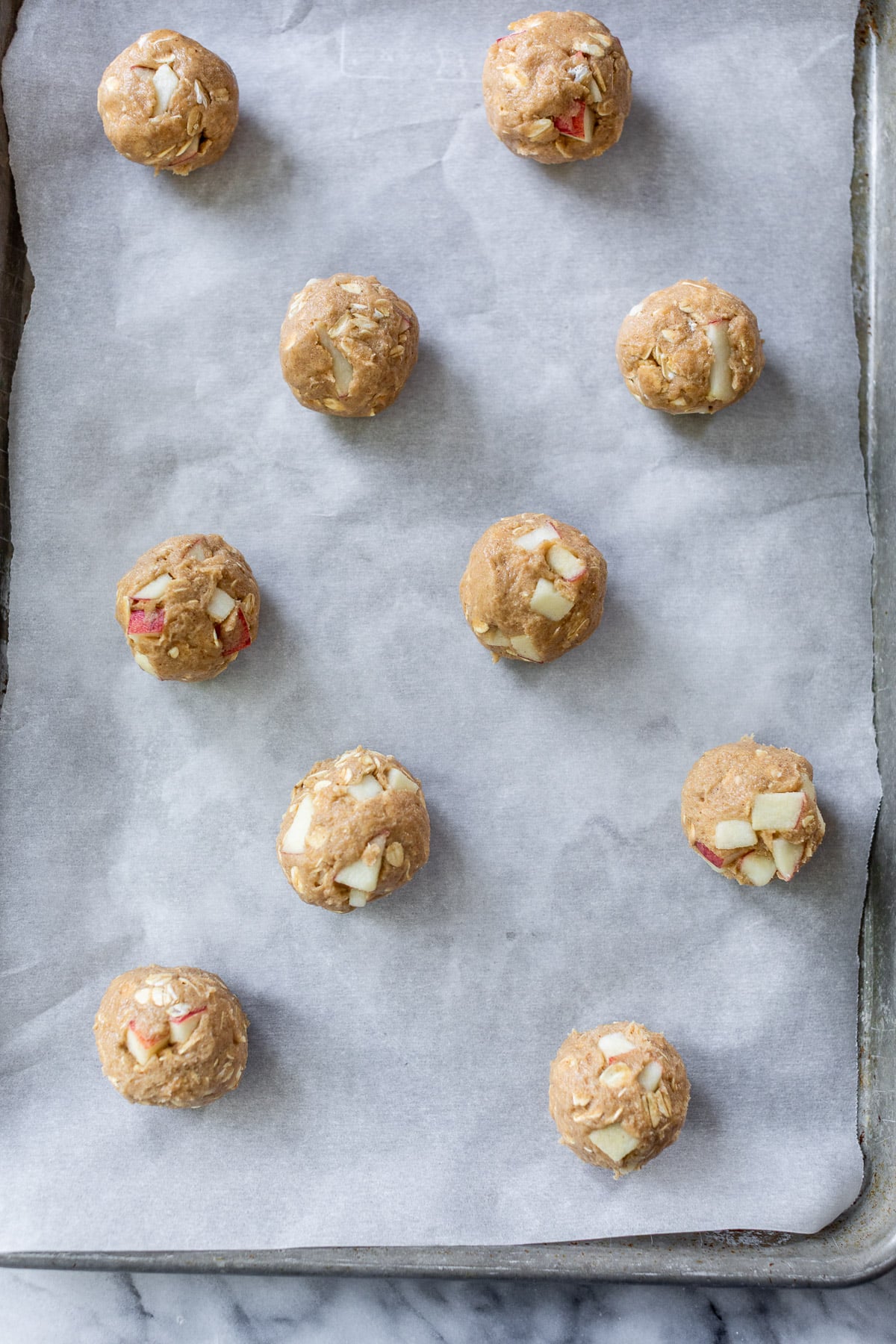 rolled unbaked apple oatmeal cookie dough balls on a parchment-lined baking sheet.