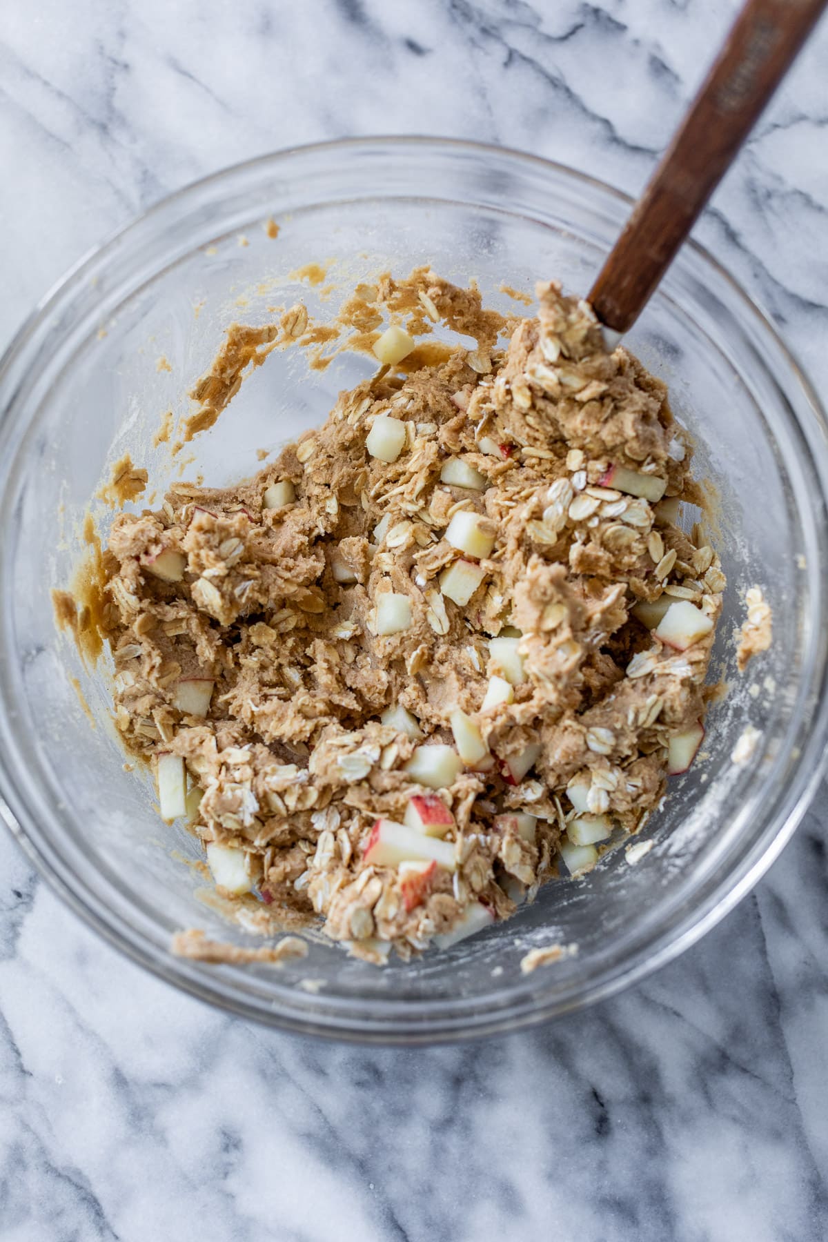 using a spatula to fold oats and apple chunks into apple oatmeal cookie dough.