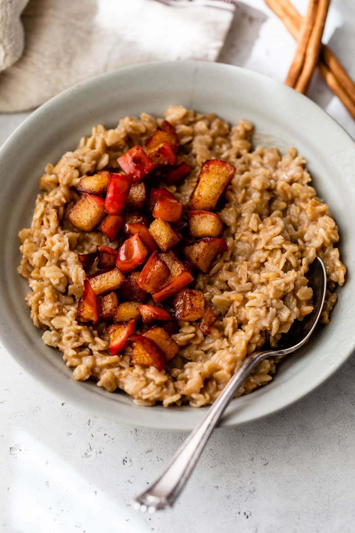 a gray-colored bowl with a spoon filled with oatmeal topped with diced cooked apple