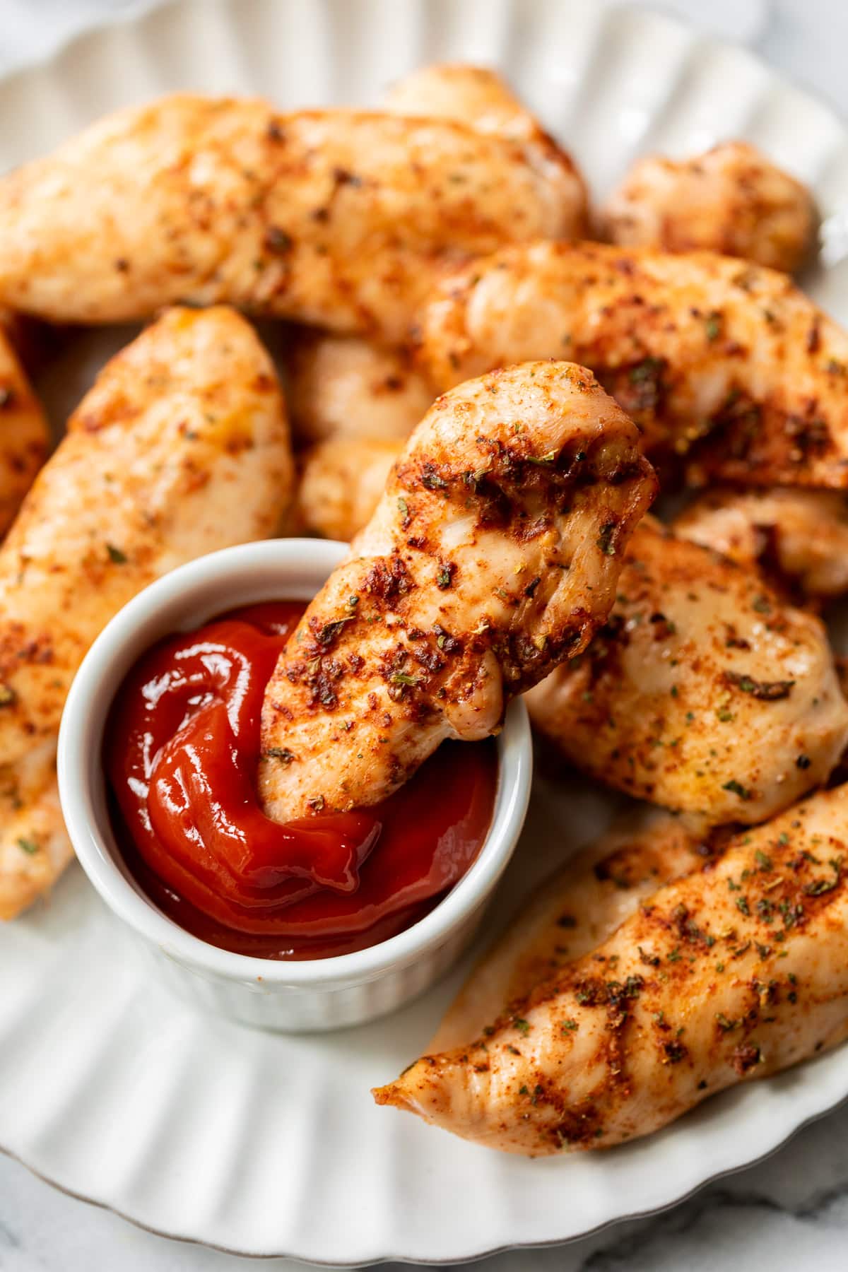 dunking a baked chicken tender into a small bowl of ketchup.
