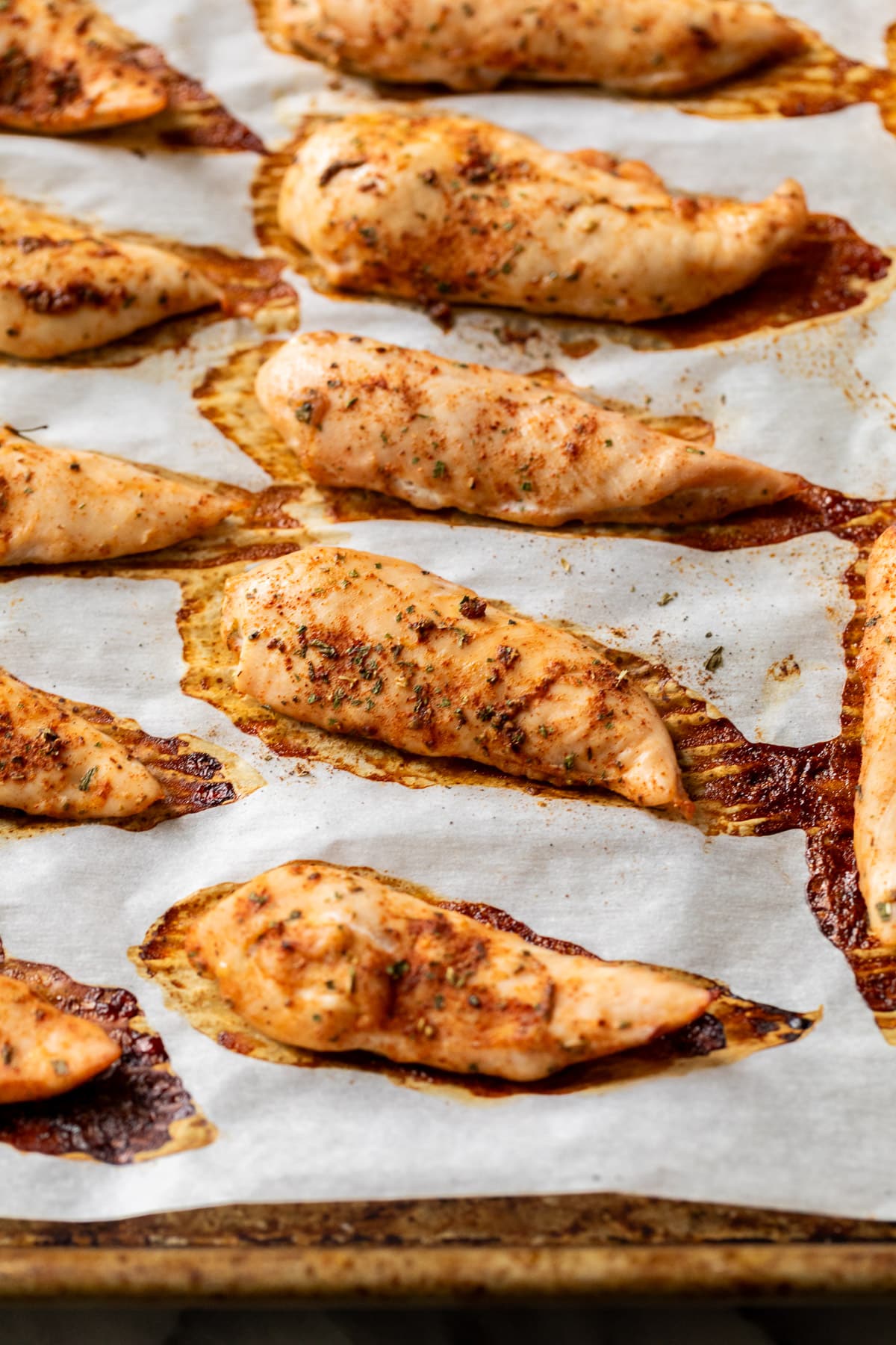 baked seasoned chicken tenders in rows on a baking sheet.