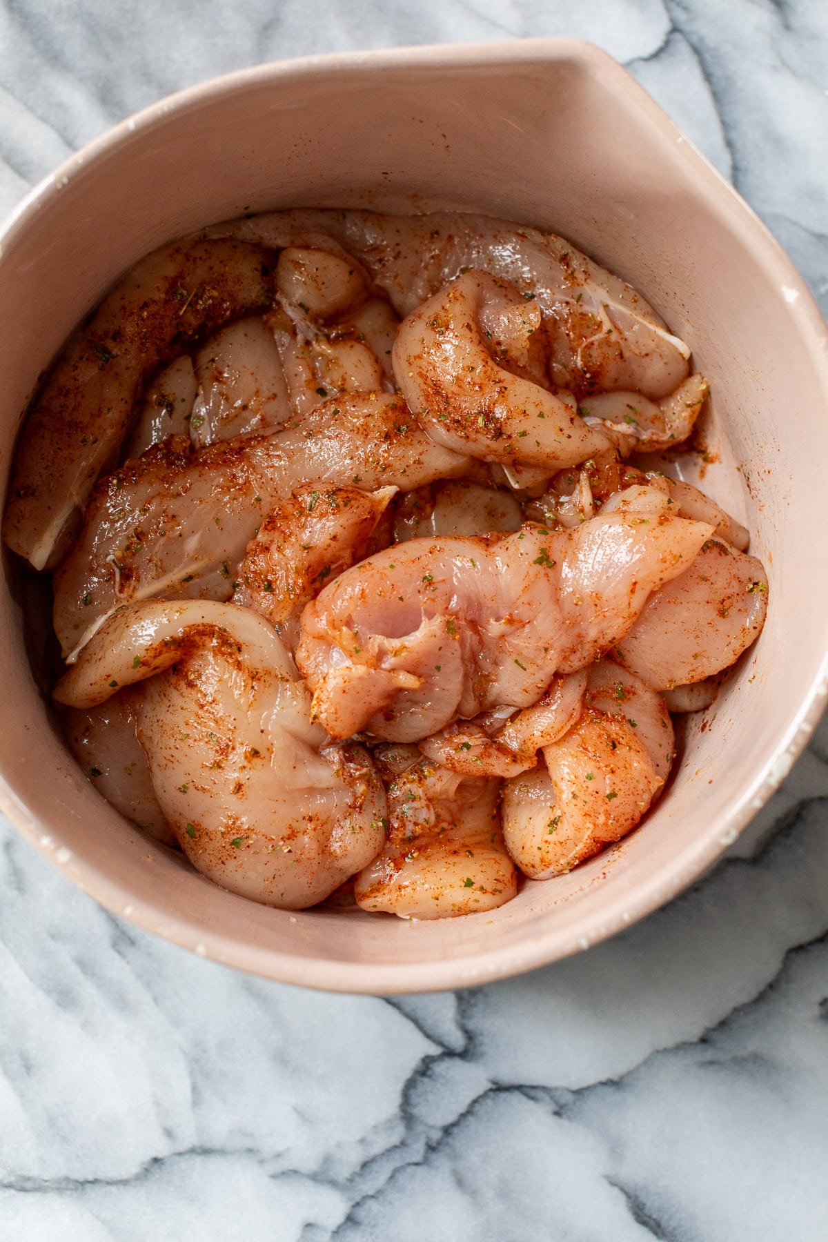 raw chicken tenders covered in seasonings in a bowl.