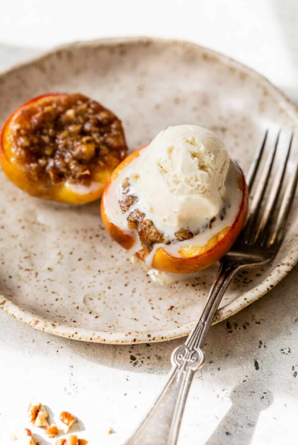 baked peaches on a plate with a fork and a scoop of vanilla ice cream on top