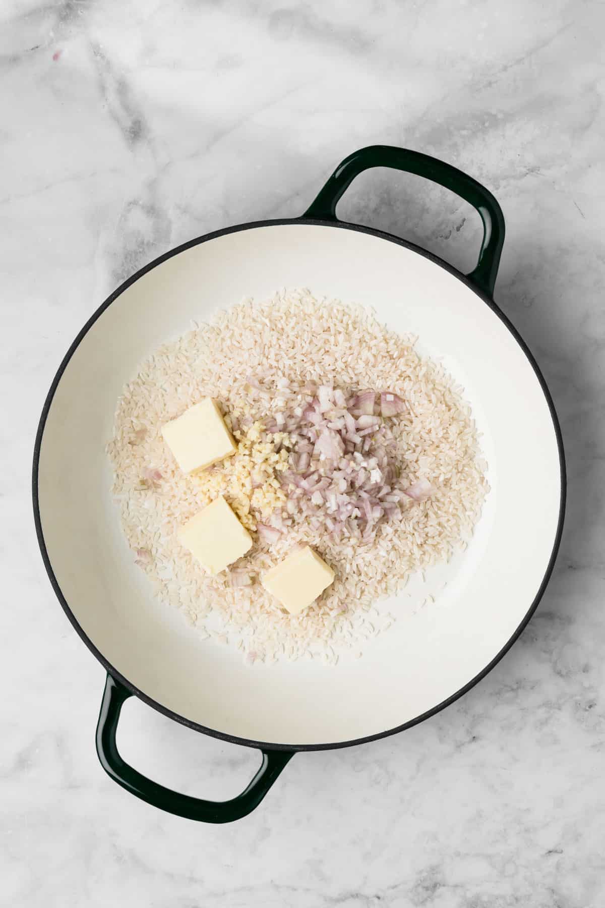 overhead view of rice, garlic, shallots, and butter in a pot for baked risotto.