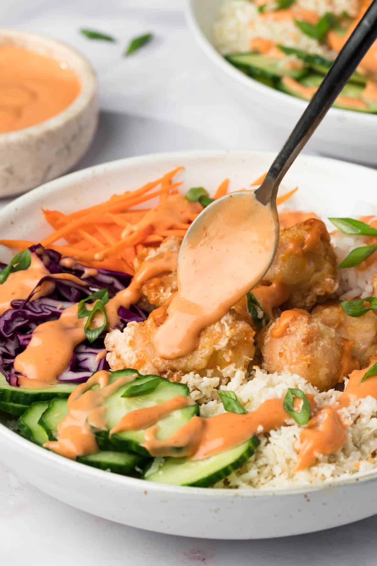 side view of a spoon drizzling bang bang sauce over a bang bang chicken bowl.