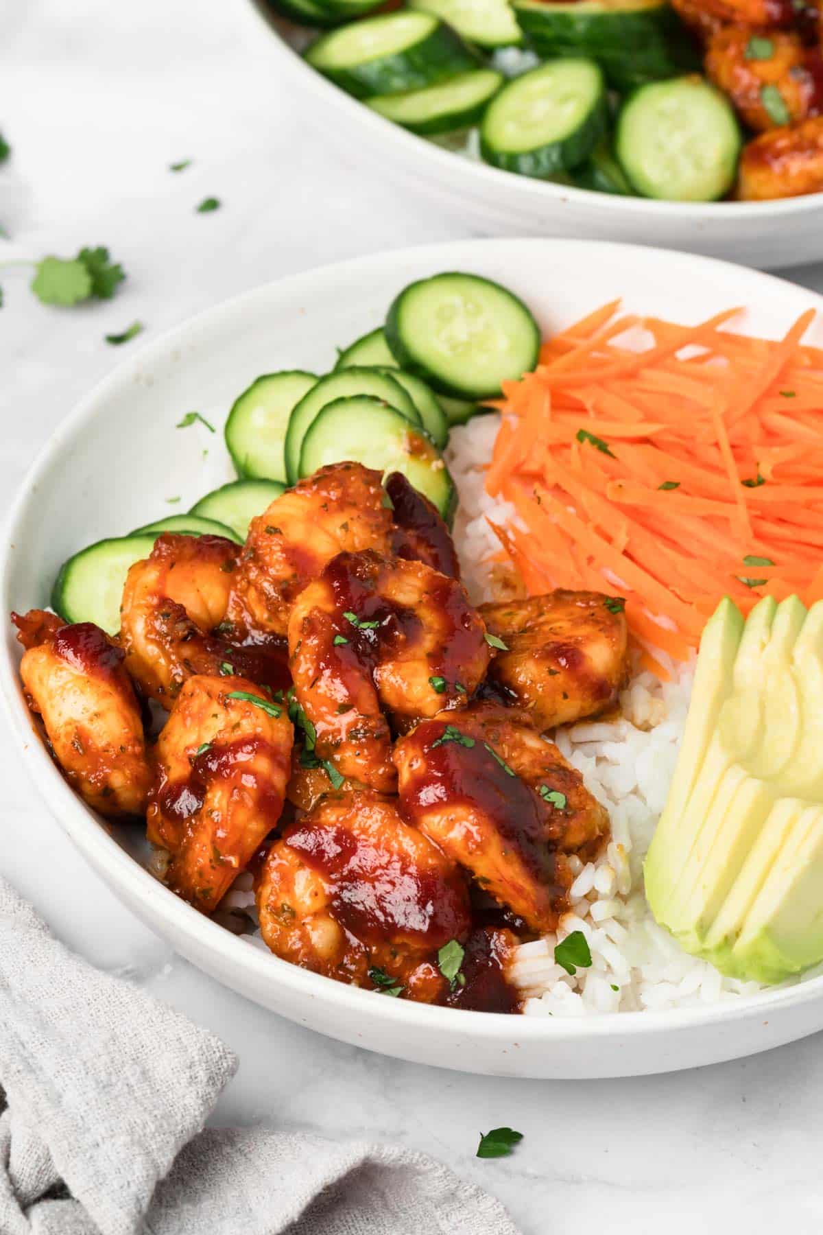side view of a BBQ Shrimp Bowl topped with shrimp, cucumbers, carrots, and avocado.