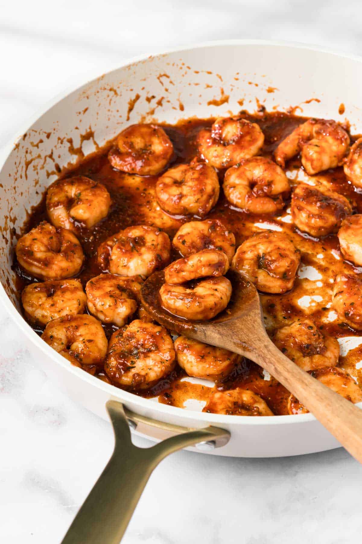 side view of cooked BBQ shrimp for BBQ shrimp bowls in a skillet with a wooden spoon.
