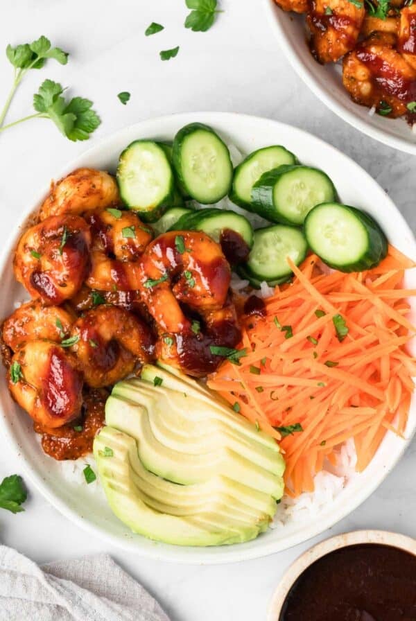 overhead view of a BBQ Shrimp Bowl topped with shrimp, cucumbers, carrots, and avocado.