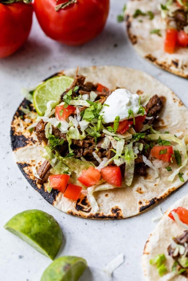 crockpot beef tacos on a tortilla with lettuce, tomatoes, and a dollop of sour cream