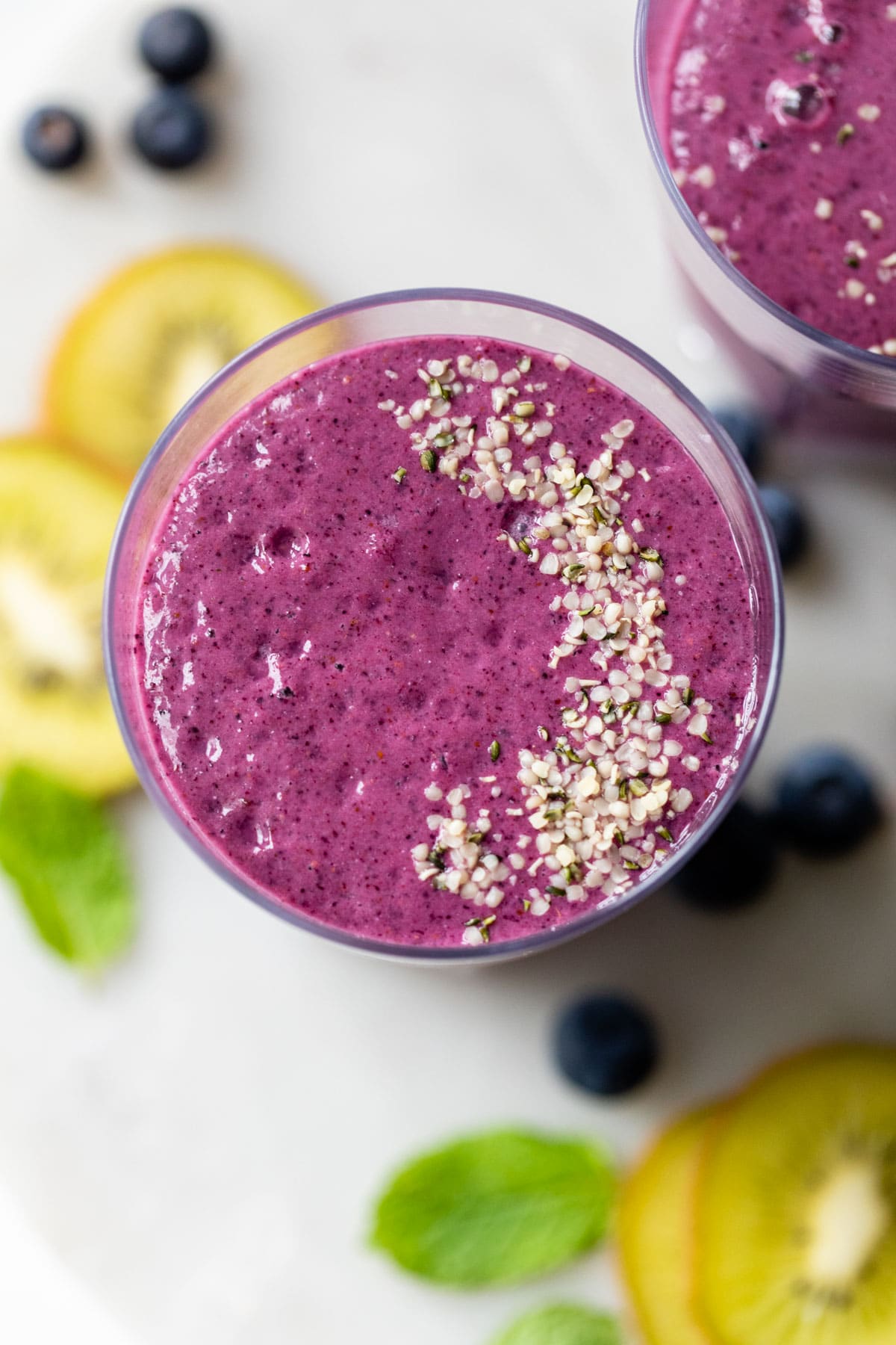 overhead photo of a blueberry smoothie in a glass beside a few sliced kiwi fruit