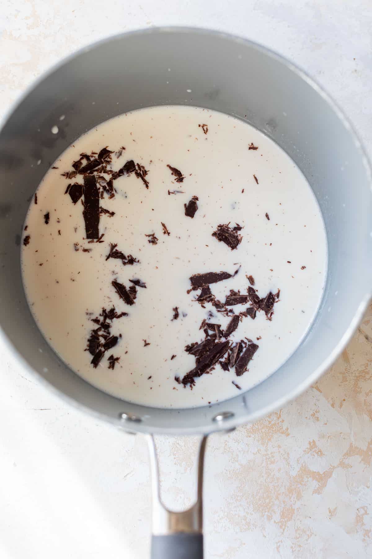 overhead view of melting chunks of chocolate in a milk mixture in a pot for boozy hot chocolate.