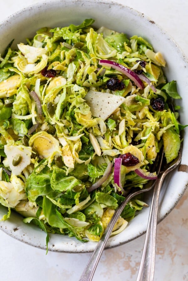 brussels sprouts slaw in a bowl with a fork and spoon
