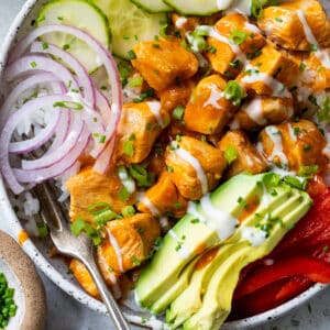 overhead view of a buffalo chicken bowl topped with buffalo chicken bites, cucumber, red onion, and avocado.
