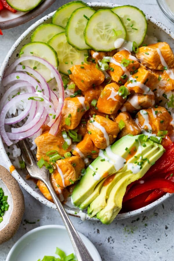 overhead view of a buffalo chicken bowl topped with buffalo chicken bites, cucumber, red onion, and avocado.