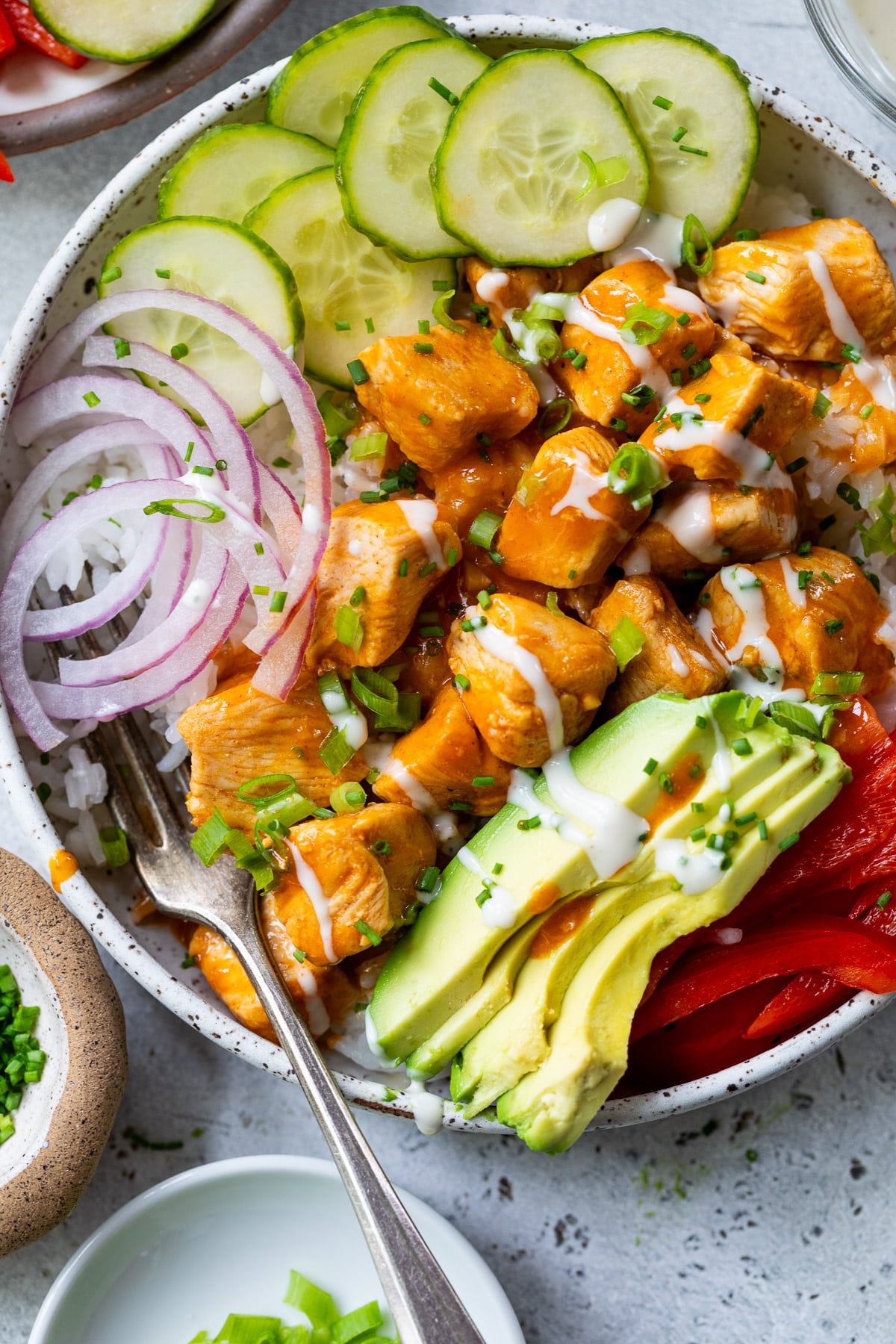 overhead view of a buffalo chicken bowl topped with buffalo chicken bites, cucumber, red onion, and avocado.