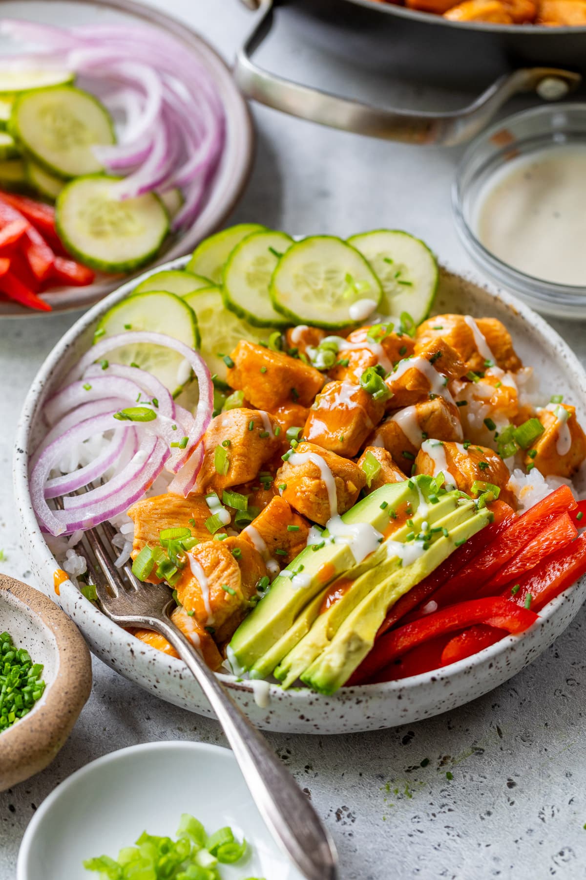 a buffalo chicken bowl topped with buffalo chicken bites, cucumber, red onion, and avocado.