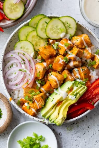 overhead view of a buffalo chicken bowl topped with buffalo chicken bites, cucumber, red onion, and avocado.