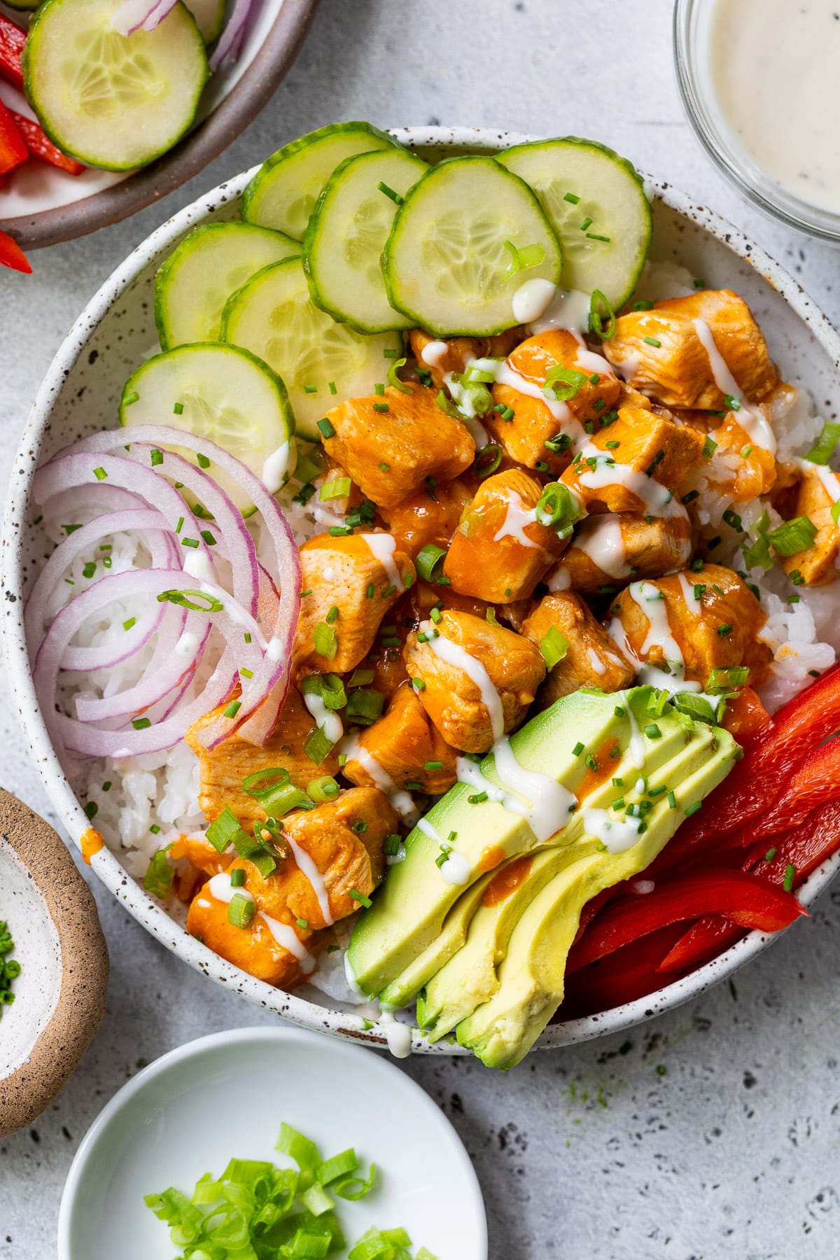overhead view of a buffalo chicken bowl topped with buffalo chicken bites, cucumber, red onion, and avocado.