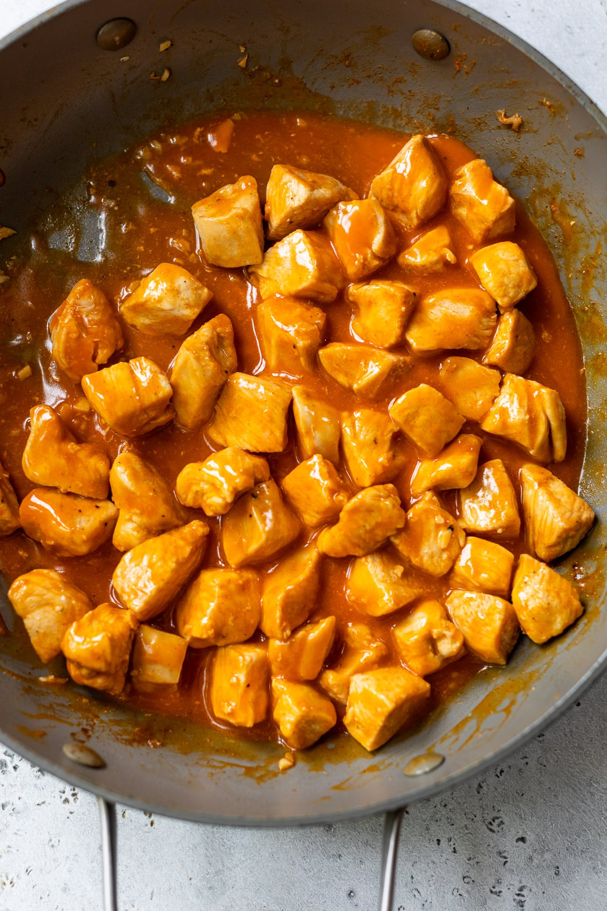 cooking chicken bites in buffalo sauce in a skillet.