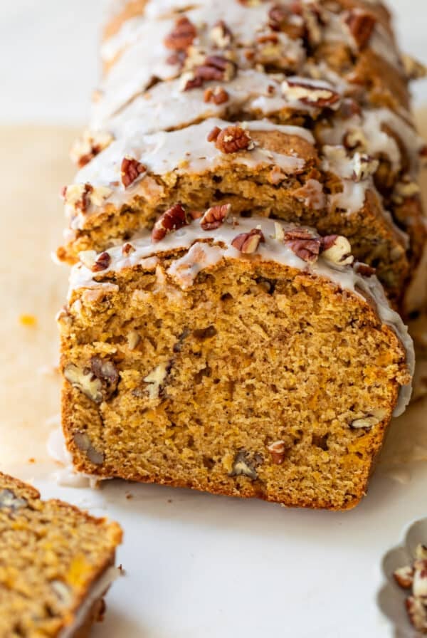overhead view of a sliced loaf of butternut squash bread topped with a white glaze and pecans.