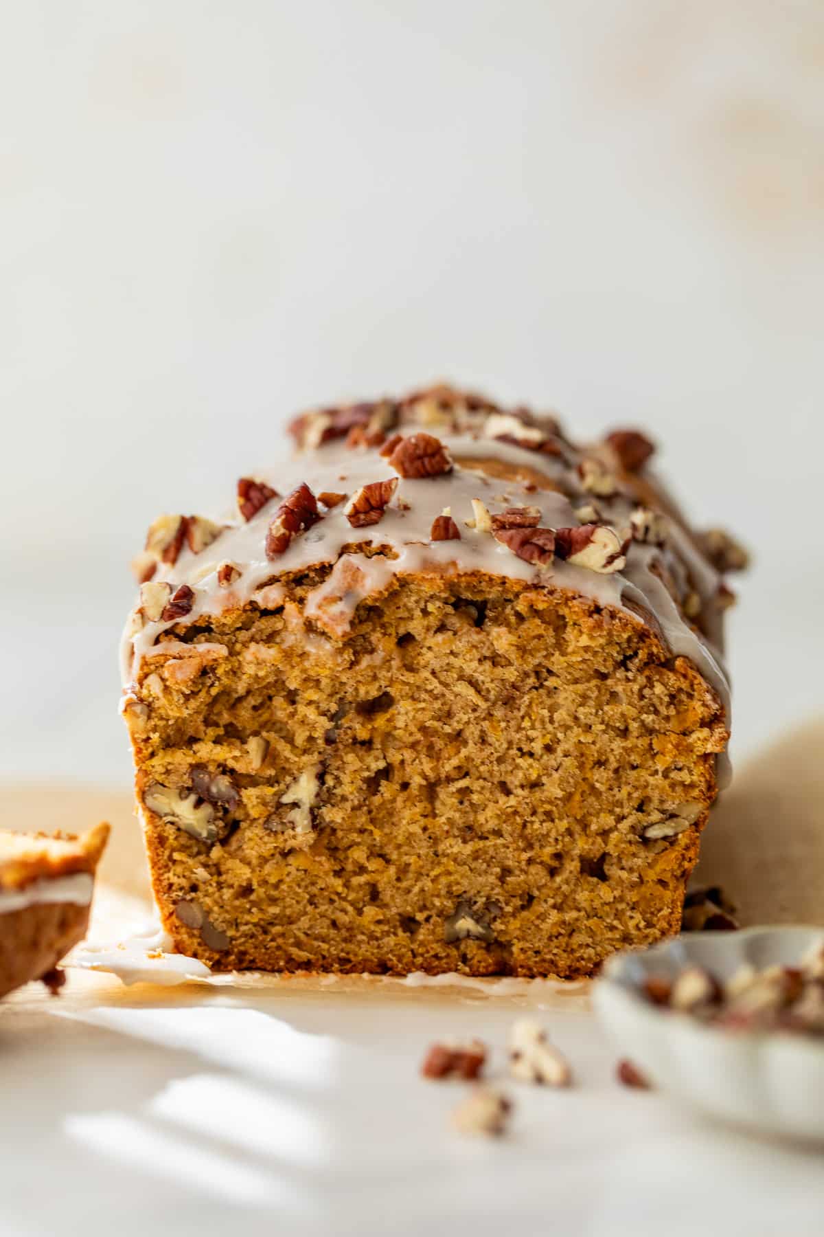 side view of a sliced loaf of butternut squash bread topped with a white glaze and pecans.
