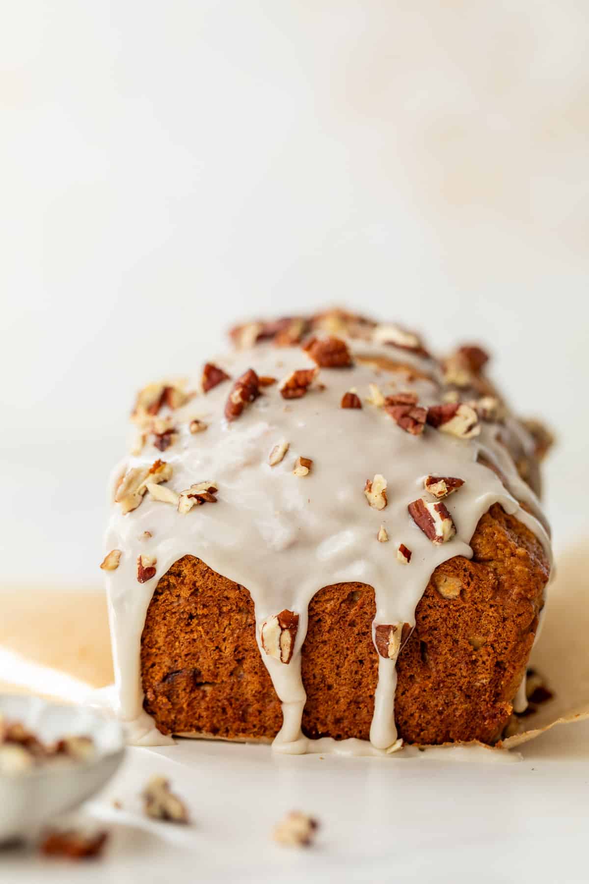 side view of a baked loaf of butternut squash bread topped with a white glaze and pecans.