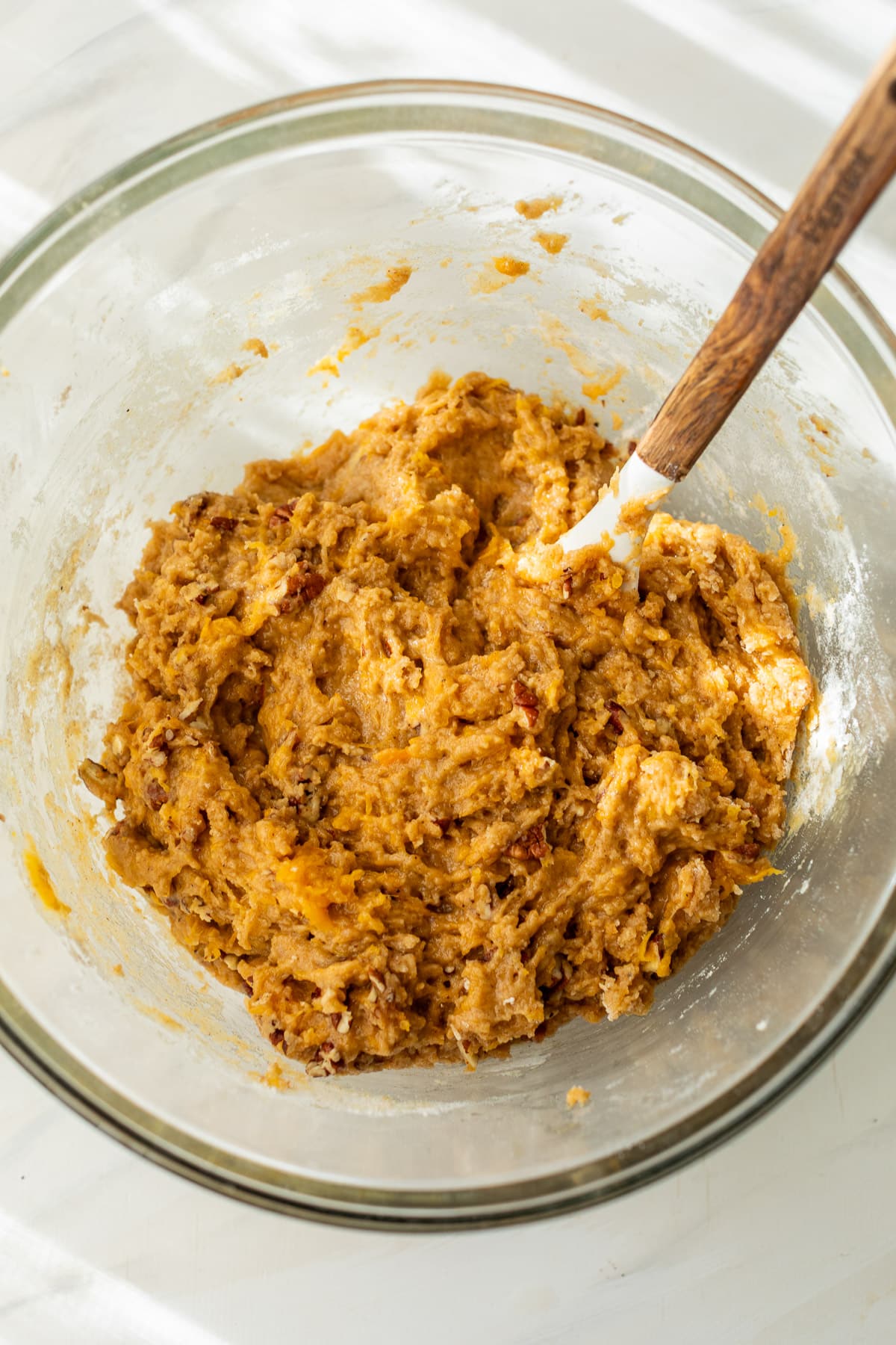 using a wooden spoon to stir the batter for butternut squash bread in a large glass bowl.