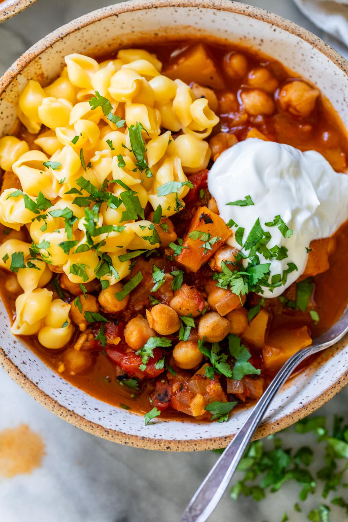 overhead view of a bowl of Butternut Squash Chickpea Chili topped with mac and cheese and sour cream.
