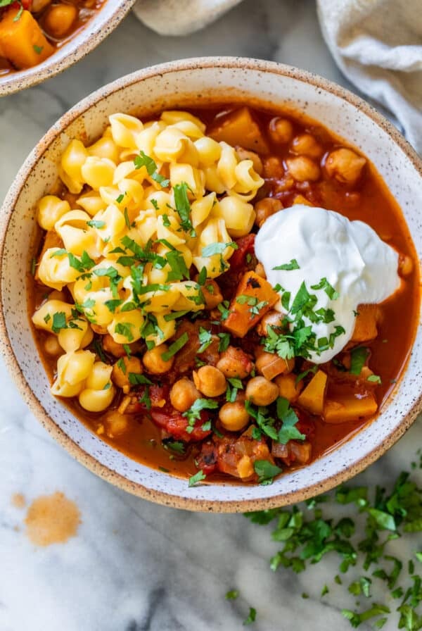 overhead view of a bowl of Butternut Squash Chickpea Chili topped with mac and cheese and sour cream.