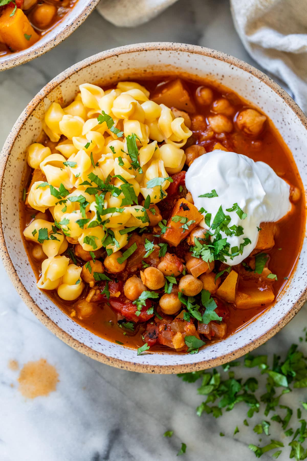overhead view of a bowl of Butternut Squash Chickpea Chili topped with mac and cheese and sour cream.