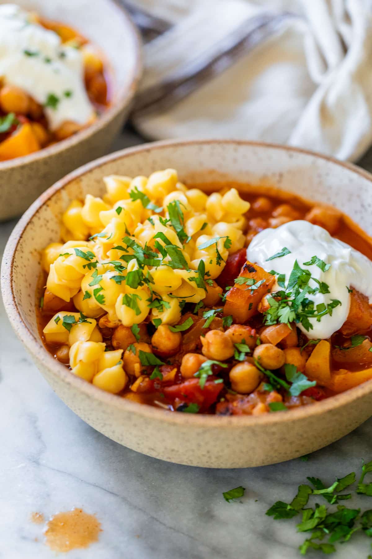 side view of a bowl of Butternut Squash Chickpea Chili topped with mac and cheese and sour cream.
