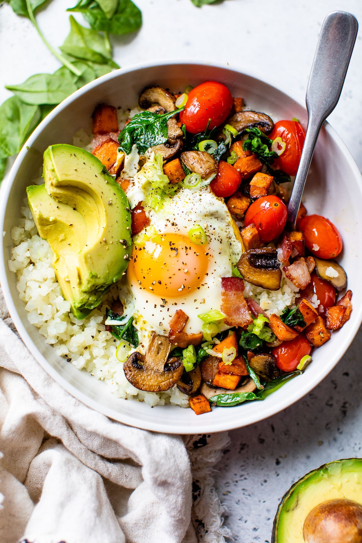 bowl filled with cauliflower rice, vegetables, avocado, and a fried egg