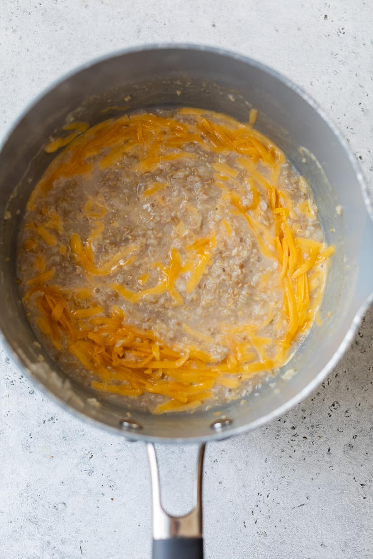 oatmeal in a saucepan with shredded cheese stirred in