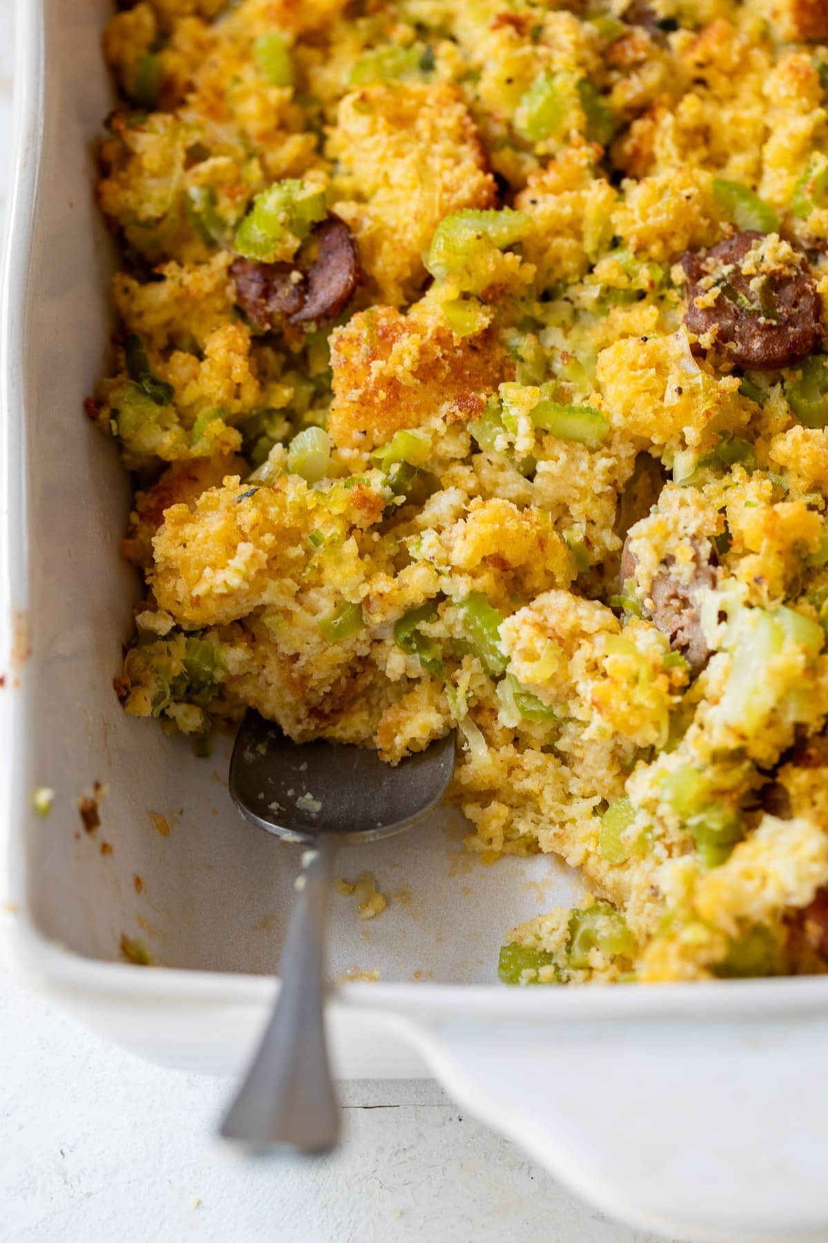 close up on a spoon in a baking dish with chicken sausage cornbread stuffing.